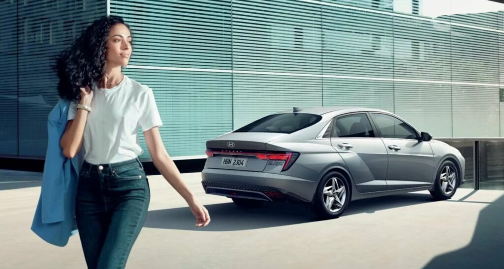 Mujer caminando con actitud segura junto a un sed&aacute;n Hyundai moderno